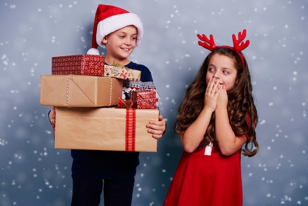 Hermanos felices con pila de regalos entre la nieve cayendo