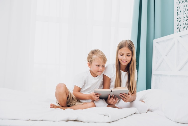 Foto gratuita hermanos de tiro largo que leen juntos un libro