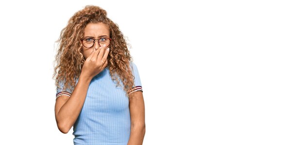 Hermosa adolescente caucásica con ropa informal y anteojos oliendo algo apestoso y repugnante olor intolerable aguantando la respiración con los dedos en la nariz mal olor