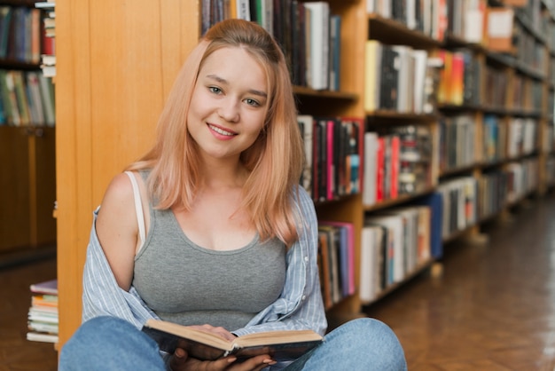 Hermosa adolescente con libro en la biblioteca