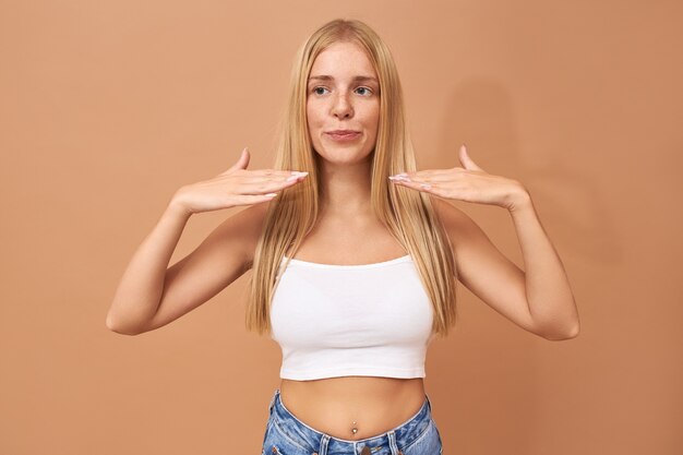 Hermosa adolescente de moda con piercing en la nariz, pecas y cabello suelto sosteniendo las palmas en la cabeza para secarse las uñas con pulidor