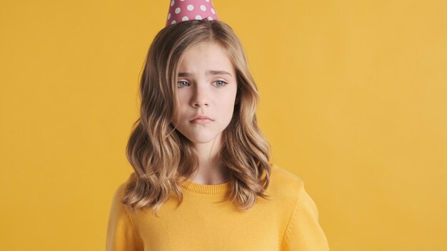 Hermosa adolescente rubia que se siente triste en su fiesta de cumpleaños aislada de fondo amarillo. Chica adolescente quiere llorar