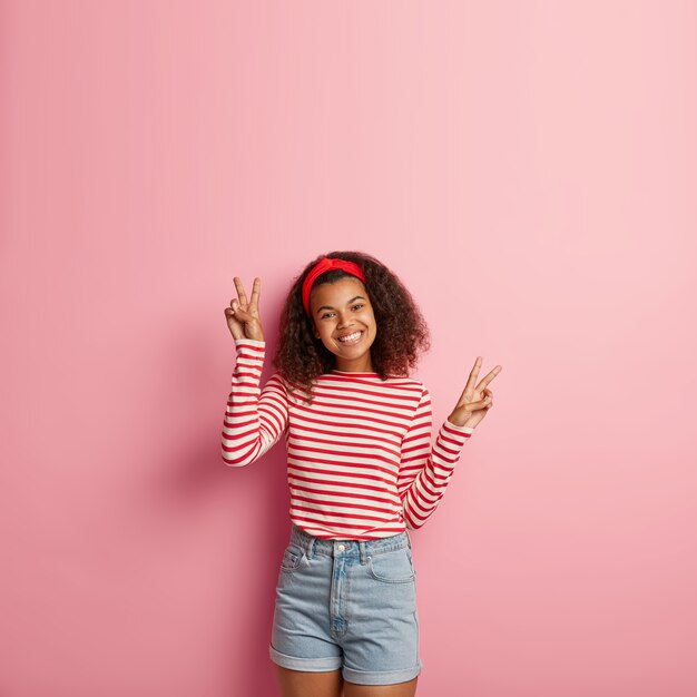 Hermosa adolescente sonriente con pelo rizado posando en suéter rojo a rayas