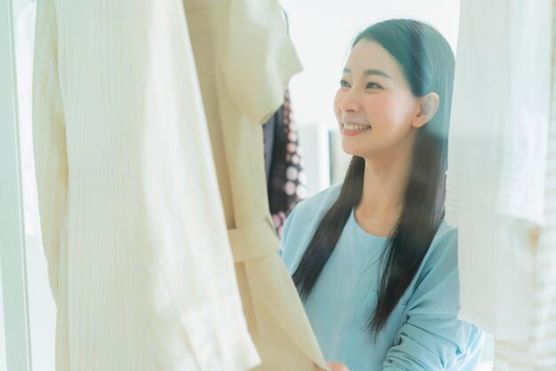 Hermosa ama de casa asiática arregla y elige tela para vestirse con luz de la mañana en un vestidor