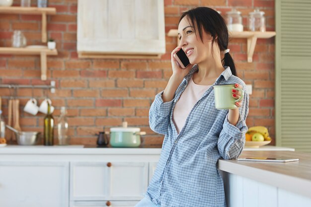 Hermosa ama de casa morena se siente aburrida en casa, charla durante mucho tiempo por teléfono inteligente