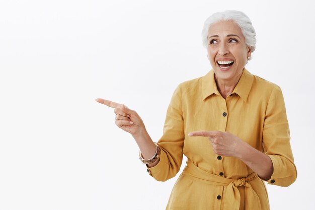 Hermosa anciana feliz riendo y señalando con el dedo a la izquierda en el anuncio