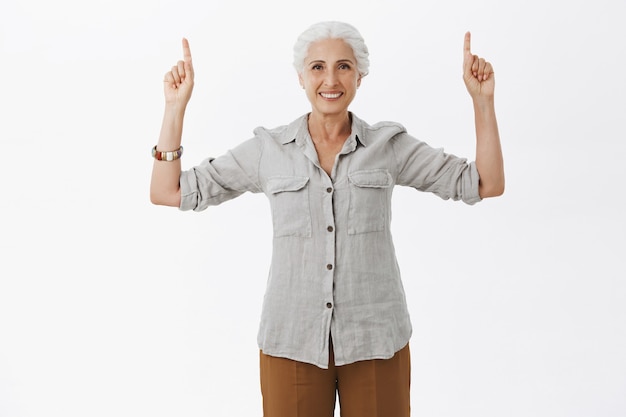 Foto gratuita hermosa anciana sonriente apuntando con el dedo hacia arriba, mostrando publicidad