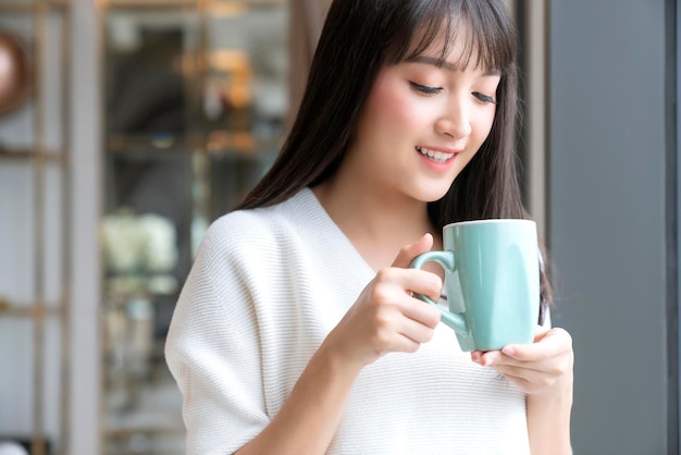 Hermosa y atractiva frescura femenina asiática sonrisa alegre mañana trabajando con café portátil desde casa con felicidad disfrutar de la vista al jardín mujer joven asiática con fondo de jardín de luz de ventana