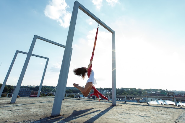 Hermosa bailarina aérea, baile de seda en el techo al amanecer