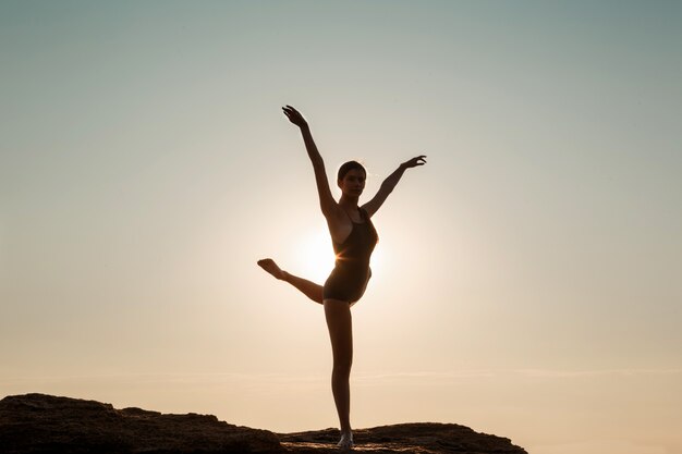 Hermosa bailarina bailando, posando en roca en la playa, vistas al mar.