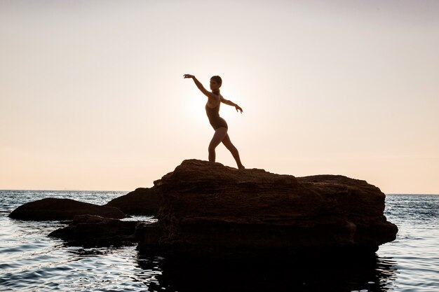 Hermosa bailarina bailando, posando en roca en la playa, vistas al mar.