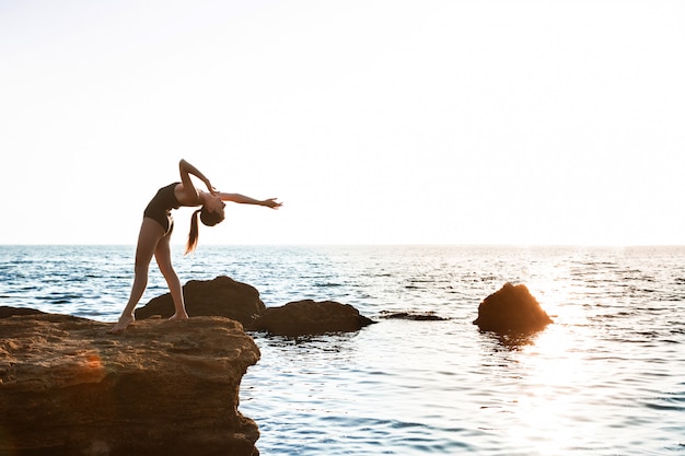 Hermosa bailarina bailando, posando en roca en la playa, vistas al mar.