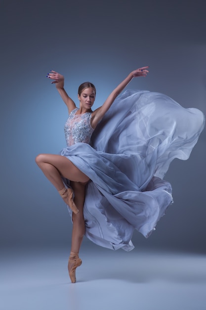 Hermosa bailarina bailando en vestido largo azul sobre fondo azul.