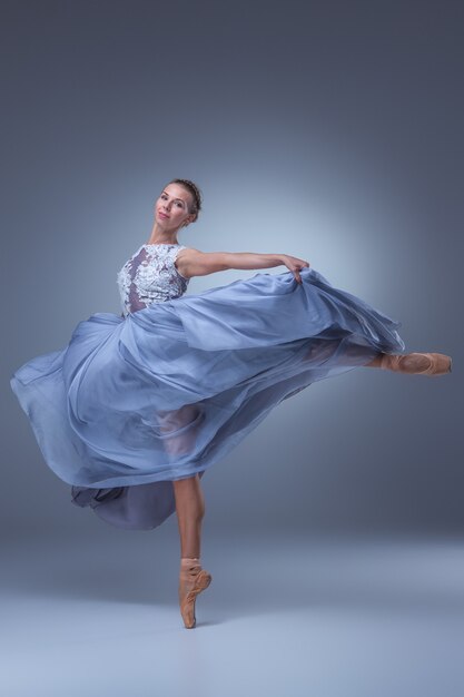 Hermosa bailarina bailando en vestido largo azul sobre fondo azul.
