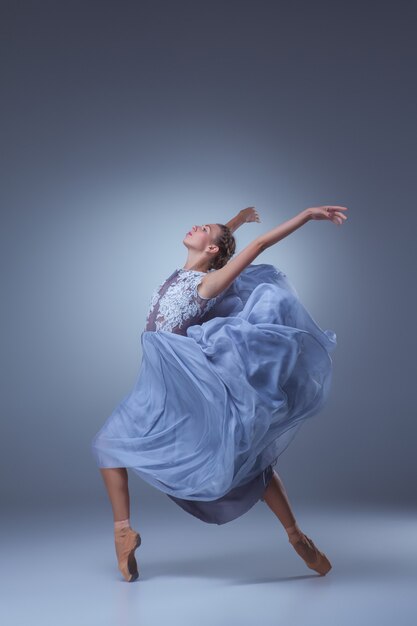 La hermosa bailarina bailando en vestido largo azul sobre fondo azul.