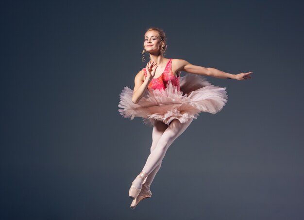 Hermosa bailarina de ballet femenino sobre un fondo gris. Bailarina lleva tutú rosa y zapatos de punta.