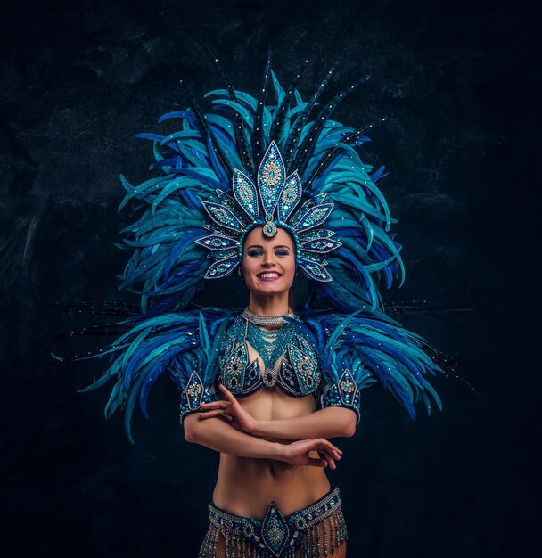 Hermosa bailarina está de pie cruza las manos. Lleva un traje de plumas azules.