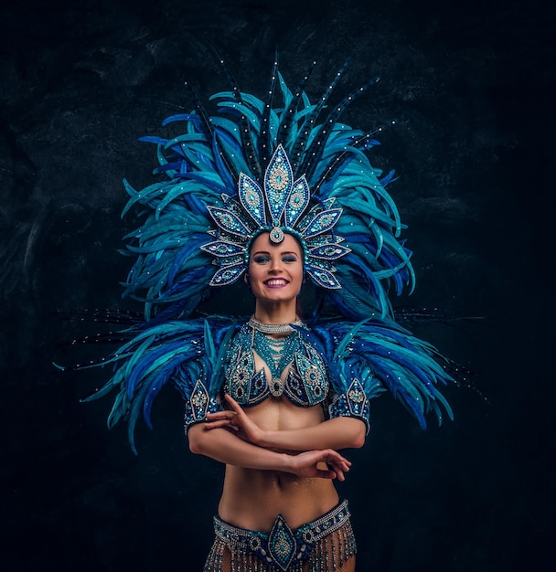 Hermosa bailarina está de pie cruza las manos. Lleva un traje de plumas azules.