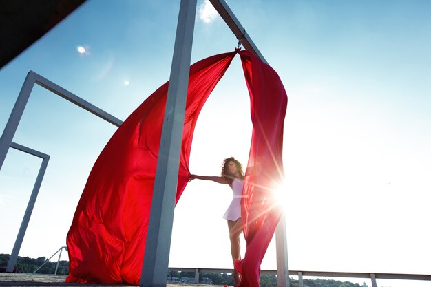 Hermosa bailarina de seda morena con cortinas rojas posando en la azotea