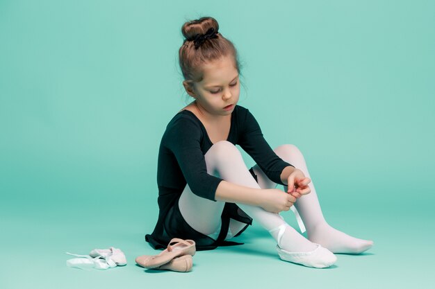 Hermosa bailarina vestida de negro para bailar sentada en el suelo y poniéndose los zapatos de punta en el estudio azul