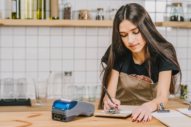 Hermosa barista escribiendo en portapapeles