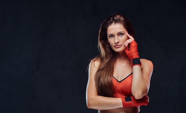 Hermosa boxeadora morena pensativa en sujetador deportivo con las manos vendadas. Aislado en un fondo de textura oscura.