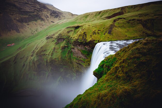 Hermosa cascada entre colinas verdes en Skogafoss, Islandia