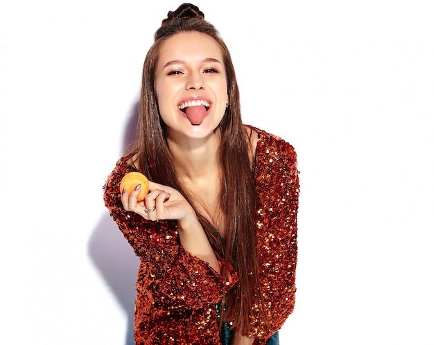 Hermosa caucásica sonriente hipster morena mujer modelo en brillante brillante reflejando verano elegante chaqueta y vestido verde aislado. Comiendo macarrones franceses y mostrando su lengua