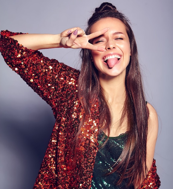 Foto gratuita hermosa caucásica sonriente hipster morena mujer modelo en brillante brillante reflejando verano elegante chaqueta y vestido verde posando en gris. mostrando signo de paz