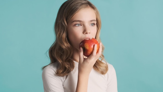 Hermosa chica adolescente rubia con cabello ondulado comiendo deliciosa manzana aislada en un fondo colorido Tiempo para la merienda