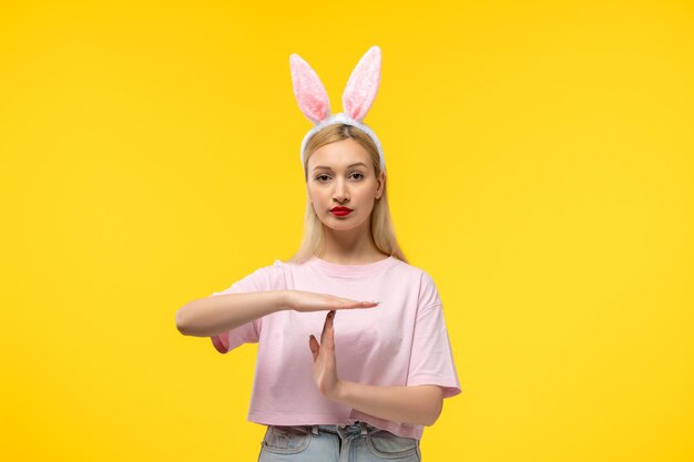 Hermosa chica adorable rubia de Pascua con orejas de conejo rosa y lápiz labial rojo que muestra la señal de stop