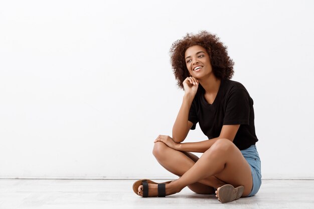 Hermosa chica africana sentada y sonriendo sobre la pared de luz.