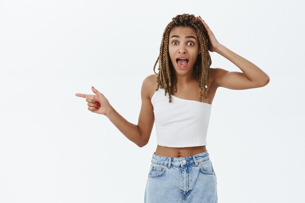 Hermosa chica afroamericana con estilo sonriendo, señalando con el dedo a la izquierda en el logo