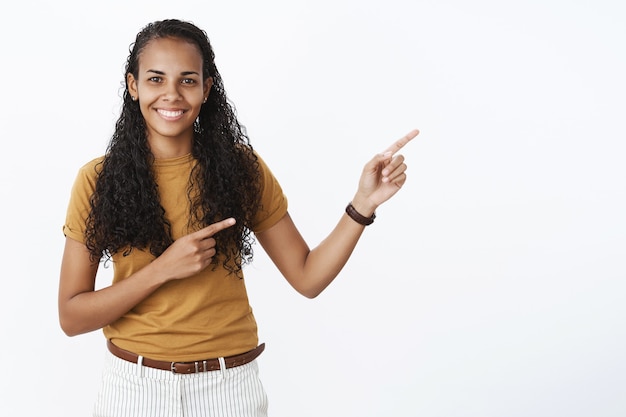 Foto gratuita hermosa chica afroamericana de pelo rizado señalando con el dedo la esquina superior derecha en el anuncio