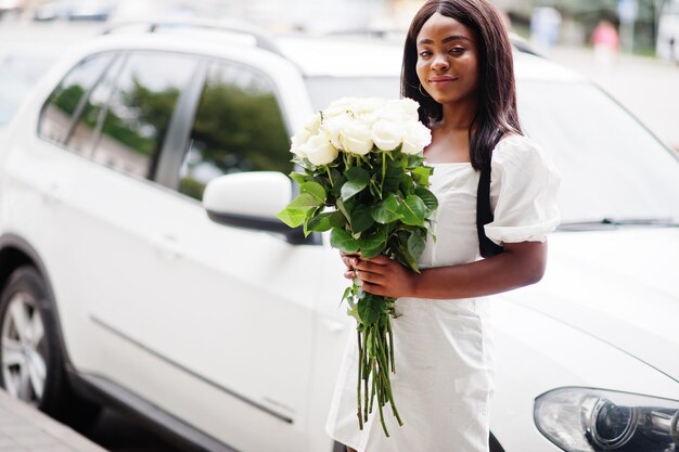 Hermosa chica afroamericana con ramo de flores de rosas blancas en citas en la ciudad Empresaria negra con ramo de flores cerca del coche