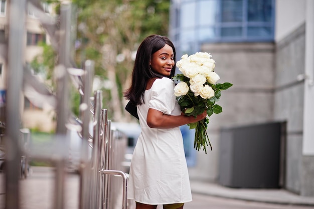 Hermosa chica afroamericana con ramo de flores de rosas blancas en citas en la ciudad Empresaria negra con ramo de flores
