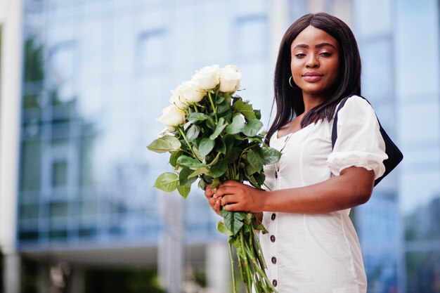 Hermosa chica afroamericana con ramo de flores de rosas blancas en citas en la ciudad Empresaria negra con ramo de flores