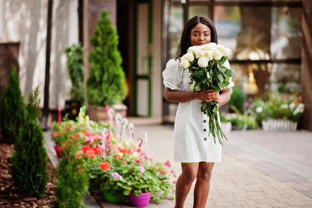 Hermosa chica afroamericana con ramo de flores de rosas blancas en citas en la ciudad Empresaria negra con ramo de flores