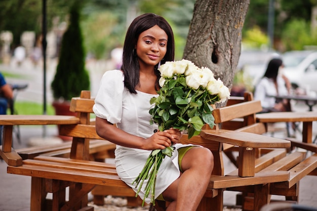 Hermosa chica afroamericana con ramo de flores de rosas blancas en citas en la ciudad Empresaria negra con ramo de flores