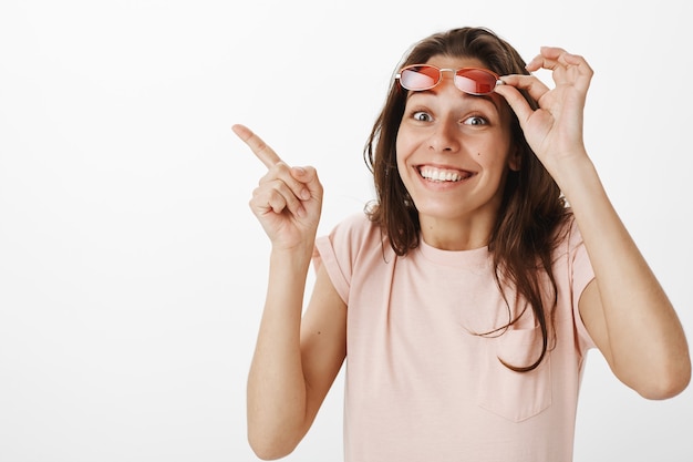 Foto gratuita hermosa chica alegre con gafas de sol posando contra la pared blanca