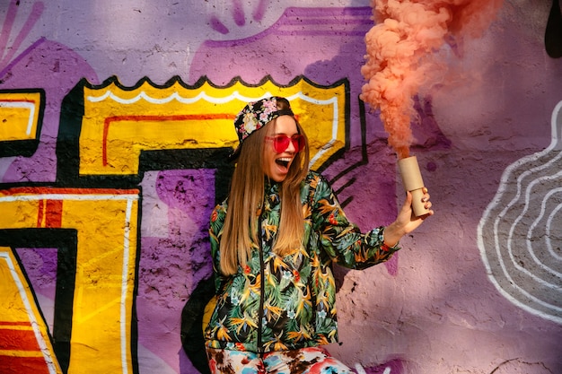 Hermosa chica alegre en ropa elegante colorido con humo bengala, que se divierte tiempo