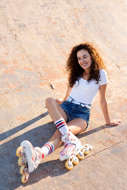 Hermosa chica de alto ángulo con el pelo rizado posando con sus patines