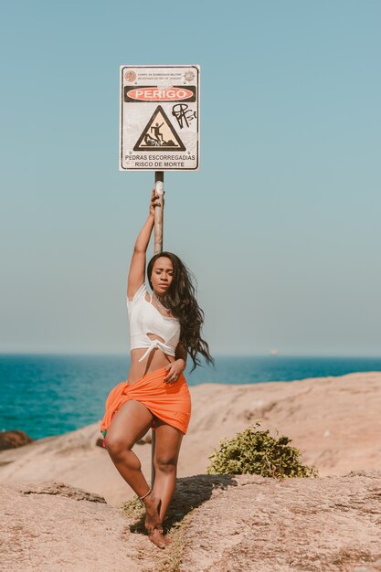 Hermosa chica apoyada contra una señal de peligro en la playa