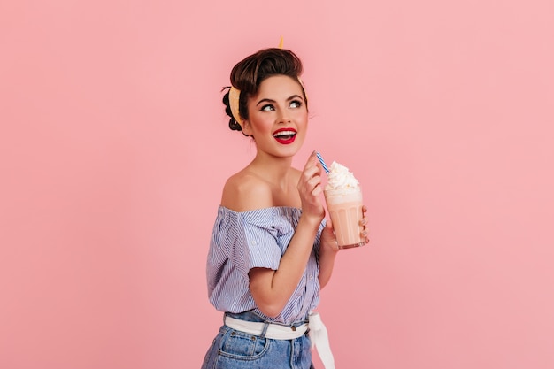 Foto gratuita hermosa chica asombrada posando con batido. mujer joven de moda disfrutando de un cóctel sobre fondo rosa.