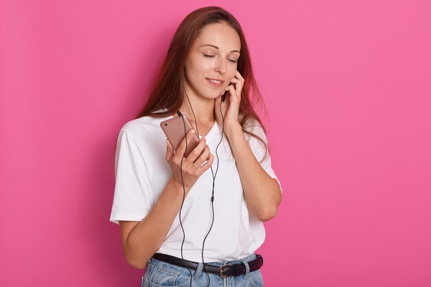 Hermosa chica en auriculares escuchando música con los ojos cerrados, de pie sobre rosa
