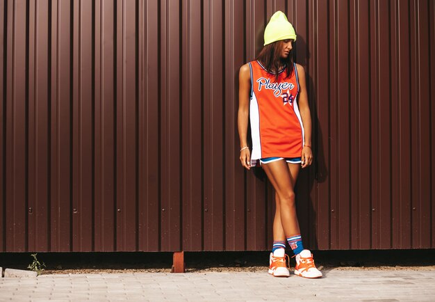 Hermosa chica en baloncesto rojo deportes posando junto a la pared metálica marrón