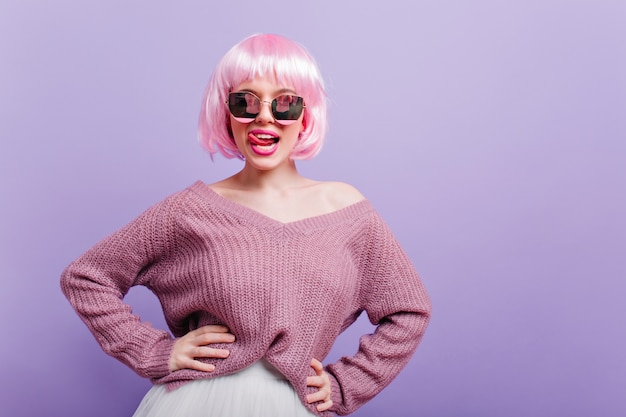 Hermosa chica blanca con peluca de moda divirtiéndose durante la sesión de fotos. Retrato de feliz modelo de mujer joven con pelo corto de color rosa de pie en pose de confianza y sonriendo.