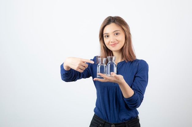 Hermosa chica en blusa azul sosteniendo un vaso de agua y apuntando a él.