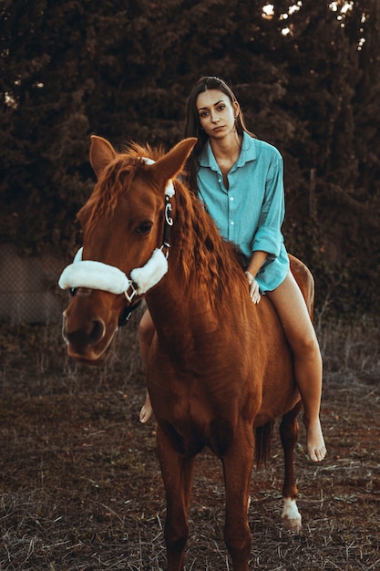 Hermosa chica en un caballo marrón afuera en soles