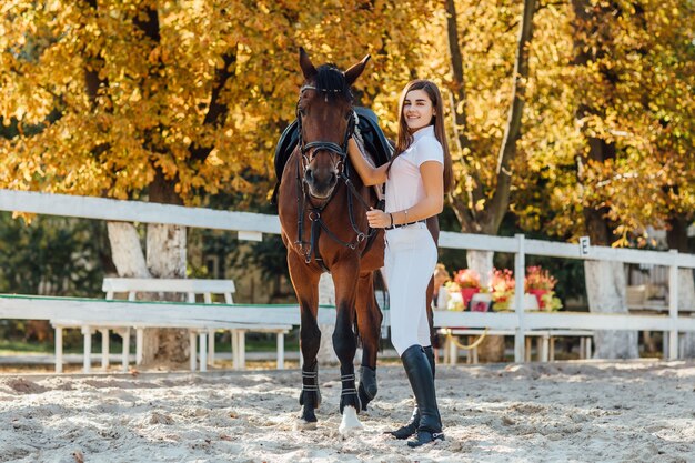 Hermosa chica con caballo marrón caminando juntos en el bosque de otoño.